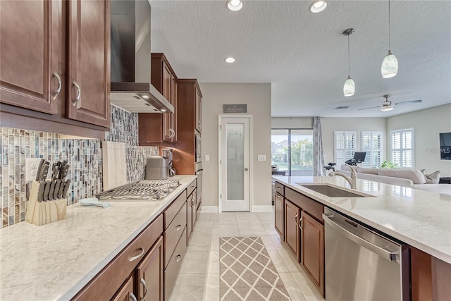 kitchen with wall chimney exhaust hood, stainless steel appliances, ceiling fan, sink, and hanging light fixtures