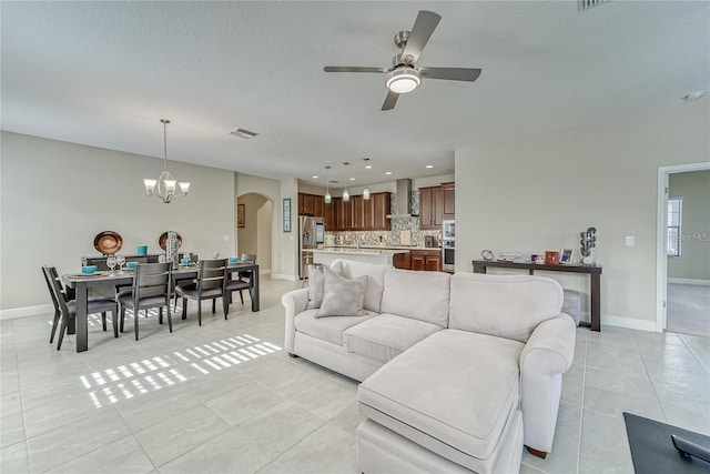 tiled living room featuring ceiling fan with notable chandelier and a textured ceiling