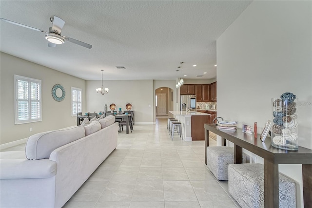 tiled living room featuring ceiling fan with notable chandelier and a textured ceiling