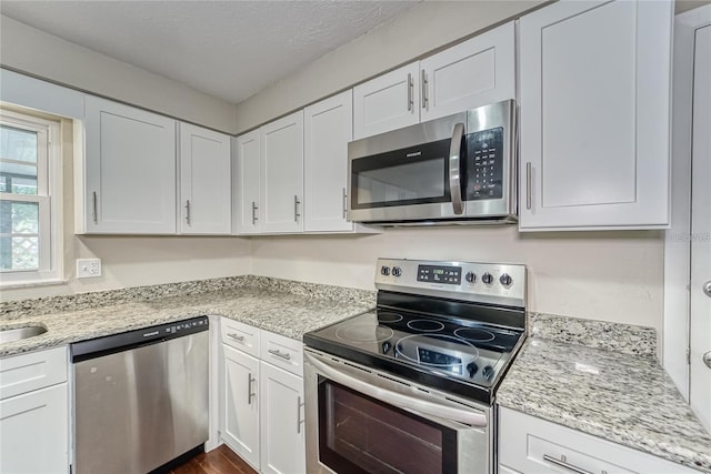 kitchen with white cabinets, light stone countertops, a textured ceiling, and appliances with stainless steel finishes