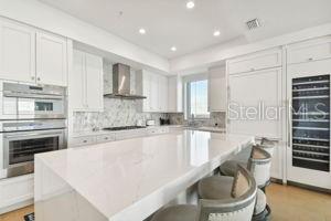 kitchen featuring a breakfast bar, a center island, wall chimney range hood, white cabinetry, and stainless steel double oven