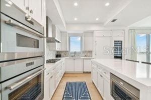 kitchen featuring gas cooktop, white cabinetry, wall chimney exhaust hood, and a healthy amount of sunlight