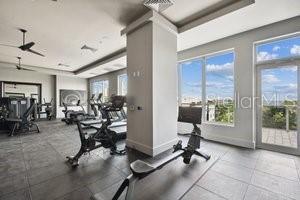 gym featuring ceiling fan, a healthy amount of sunlight, and a raised ceiling