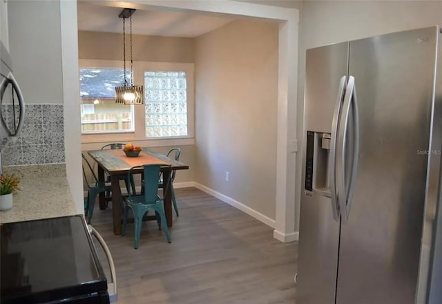 kitchen featuring hanging light fixtures, stainless steel fridge, hardwood / wood-style floors, decorative backsplash, and range