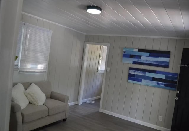 sitting room with wood walls, ornamental molding, and dark wood-type flooring