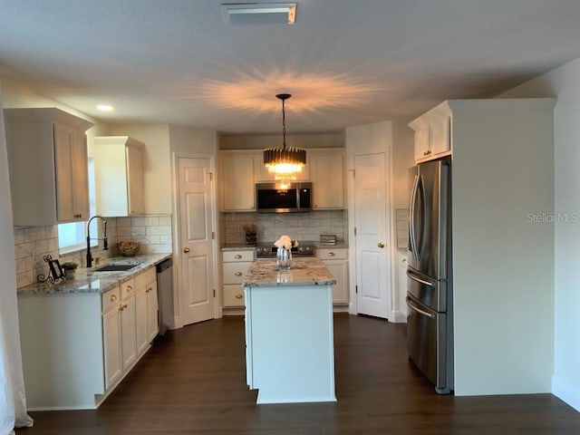 kitchen with stainless steel appliances, sink, decorative light fixtures, white cabinetry, and a kitchen island