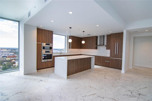 kitchen featuring pendant lighting, sink, double oven, a kitchen island, and wall chimney exhaust hood