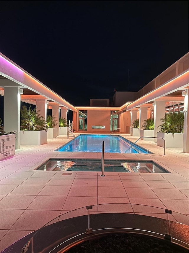 pool at night with an in ground hot tub and a patio area