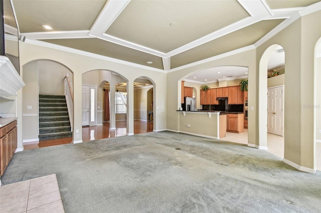 unfurnished living room with ornamental molding, light colored carpet, and a tray ceiling