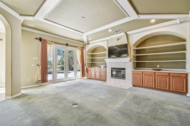 unfurnished living room with built in features, ornamental molding, a textured ceiling, light colored carpet, and french doors