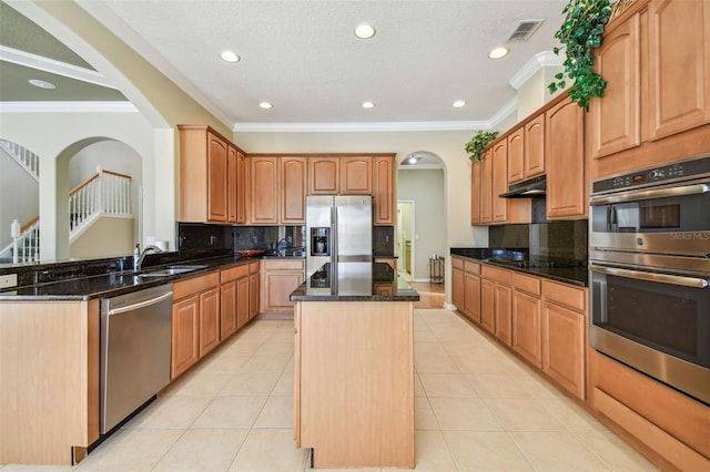 kitchen featuring sink, stainless steel appliances, a center island, ornamental molding, and dark stone counters