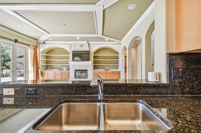 kitchen featuring sink, crown molding, built in features, and dark stone counters