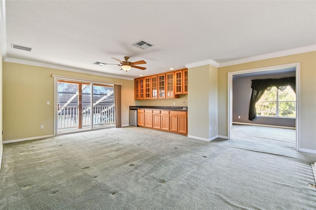 unfurnished living room with crown molding, carpet floors, bar area, and ceiling fan