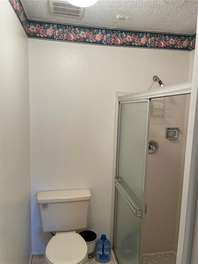 bathroom with toilet, a shower with shower door, and a textured ceiling