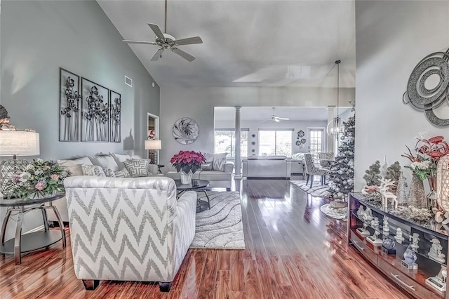 living room featuring ceiling fan with notable chandelier, wood-type flooring, high vaulted ceiling, and decorative columns