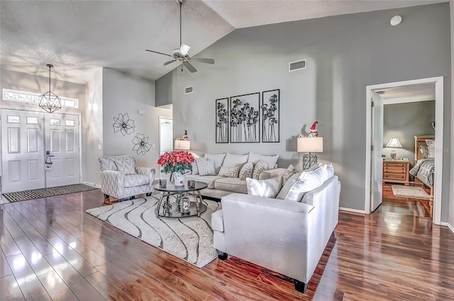 living room with ceiling fan with notable chandelier, dark hardwood / wood-style flooring, a textured ceiling, and high vaulted ceiling