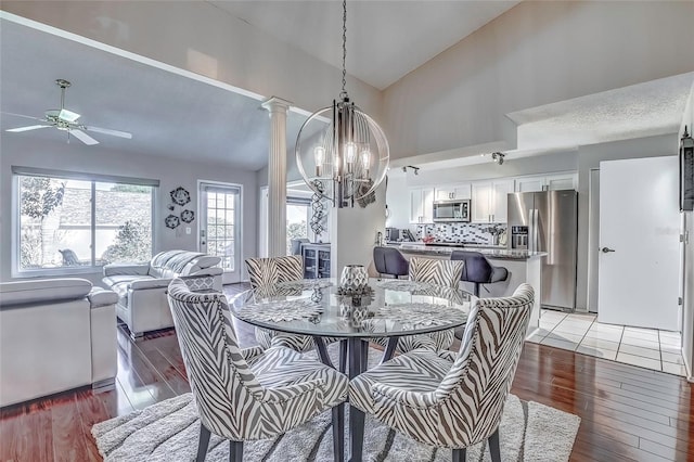 dining space with ceiling fan with notable chandelier, hardwood / wood-style flooring, high vaulted ceiling, and decorative columns