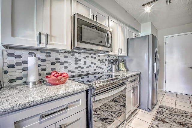 kitchen with backsplash, light tile patterned floors, a textured ceiling, light stone counters, and stainless steel appliances