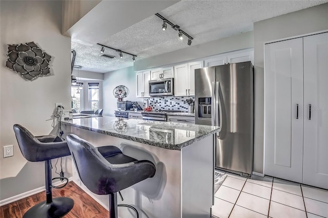 kitchen featuring appliances with stainless steel finishes, a kitchen breakfast bar, track lighting, dark stone countertops, and white cabinetry