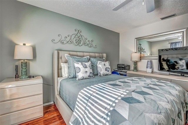 bedroom with a textured ceiling, ceiling fan, and dark hardwood / wood-style floors