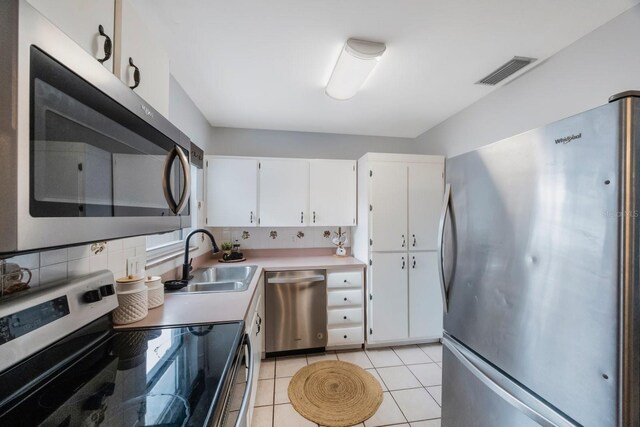 kitchen featuring sink, decorative backsplash, light tile patterned flooring, white cabinetry, and stainless steel appliances