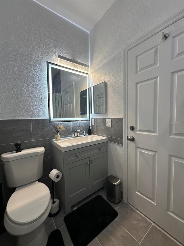 bathroom with tile patterned flooring, vanity, toilet, and tile walls