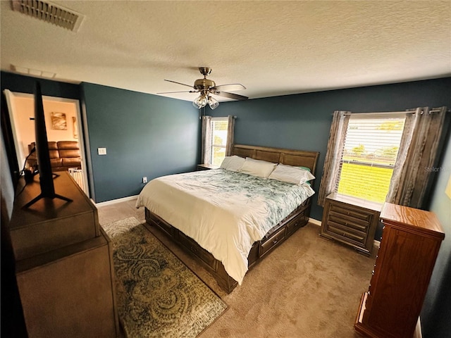 carpeted bedroom with a textured ceiling, multiple windows, and ceiling fan