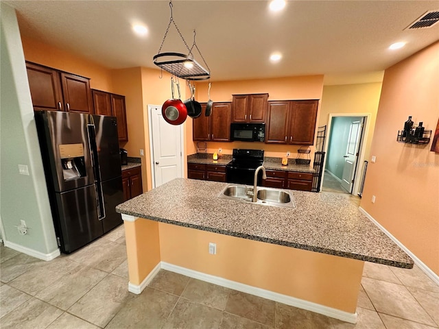 kitchen featuring a kitchen bar, dark brown cabinets, a kitchen island with sink, sink, and black appliances