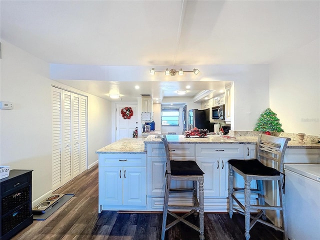 kitchen featuring light stone countertops, black refrigerator, dark hardwood / wood-style flooring, a breakfast bar, and white cabinets