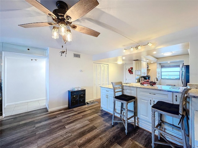 kitchen with stainless steel refrigerator, light stone counters, dark hardwood / wood-style floors, a breakfast bar area, and white cabinets