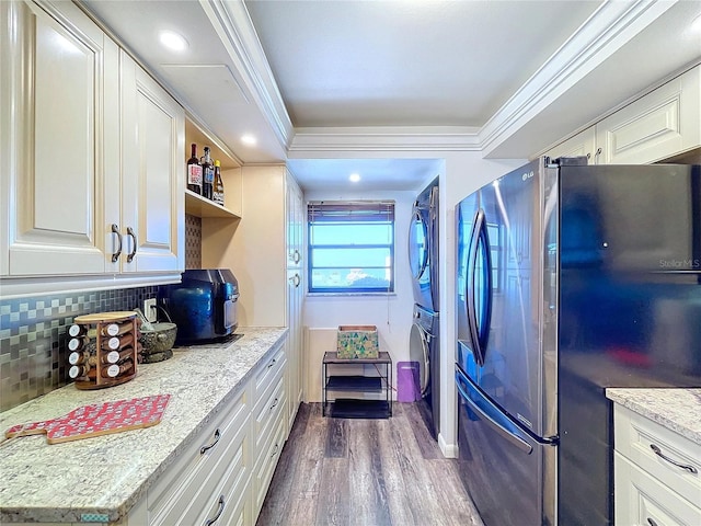 kitchen with stainless steel refrigerator, white cabinetry, stacked washer / dryer, and decorative backsplash