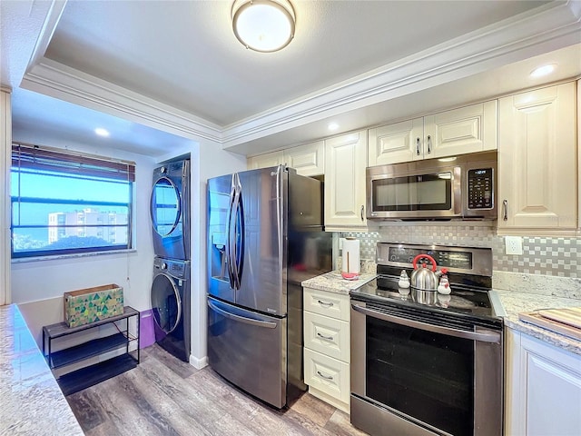 kitchen featuring ornamental molding, stainless steel appliances, light hardwood / wood-style flooring, and stacked washer and clothes dryer