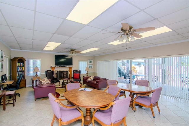 dining space with a ceiling fan, a paneled ceiling, a fireplace, and light tile patterned floors