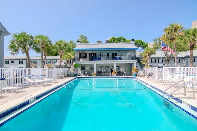 community pool with a patio area, fence, and stairway