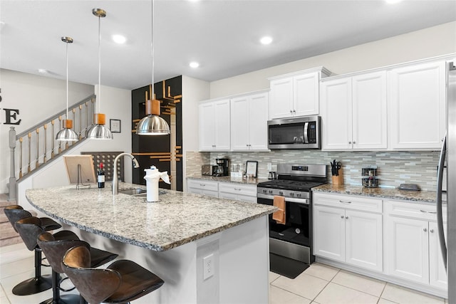 kitchen with backsplash, hanging light fixtures, appliances with stainless steel finishes, and an island with sink