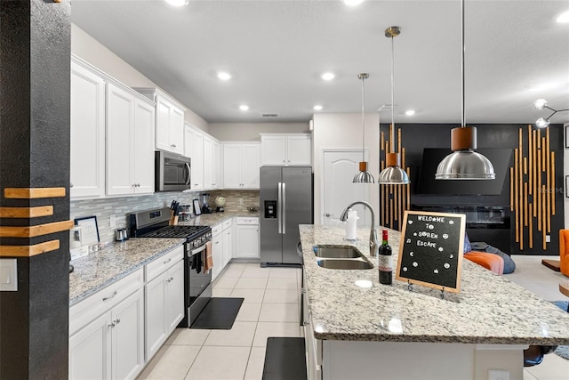 kitchen with sink, hanging light fixtures, stainless steel appliances, a kitchen island with sink, and white cabinets