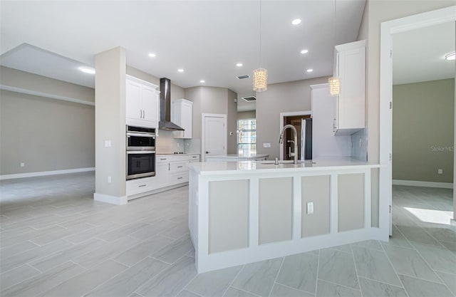 kitchen featuring white cabinetry, sink, wall chimney exhaust hood, double oven, and decorative light fixtures