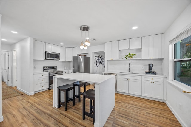 kitchen with appliances with stainless steel finishes, a breakfast bar, sink, pendant lighting, and white cabinets