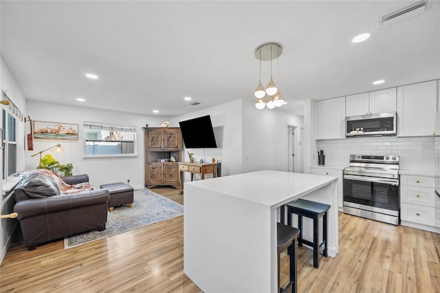 kitchen with white cabinetry, a center island, stainless steel appliances, light hardwood / wood-style floors, and decorative light fixtures