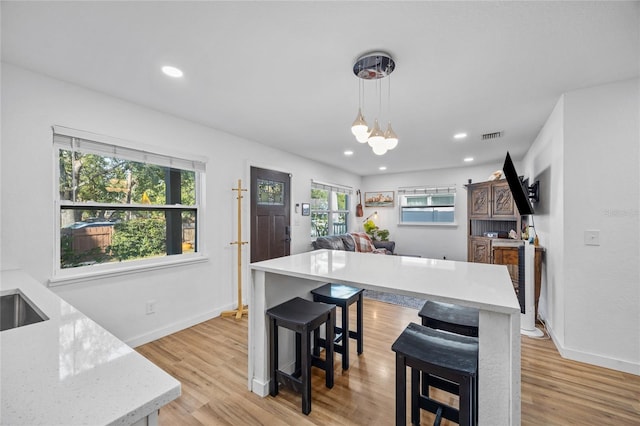 kitchen with hanging light fixtures, light hardwood / wood-style flooring, light stone countertops, a notable chandelier, and a kitchen bar