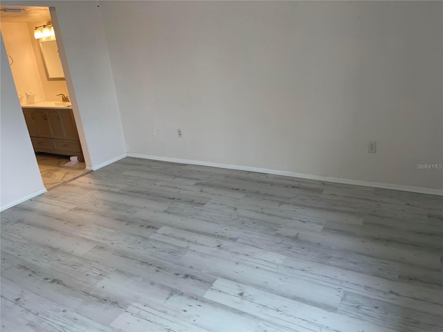 unfurnished bedroom with light wood finished floors, ensuite bath, a sink, and baseboards