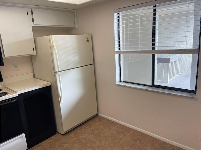 kitchen featuring light countertops, electric range, freestanding refrigerator, white cabinets, and baseboards