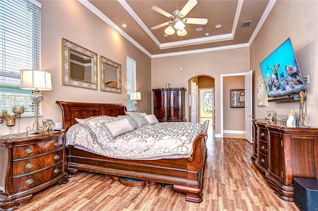 bedroom featuring ceiling fan, a raised ceiling, crown molding, and light hardwood / wood-style flooring