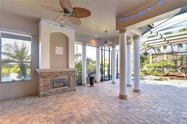 view of patio with a lanai, a stone fireplace, and ceiling fan