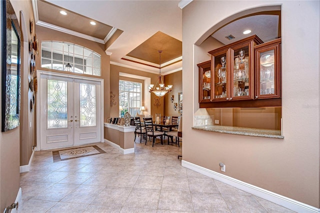 foyer entrance featuring light tile patterned flooring, french doors, crown molding, and a notable chandelier