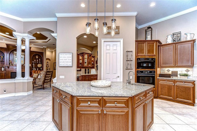 kitchen with decorative columns, a kitchen island with sink, light stone countertops, and ornamental molding