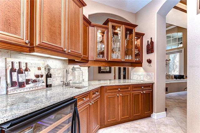 kitchen featuring backsplash, sink, light stone countertops, light tile patterned floors, and beverage cooler