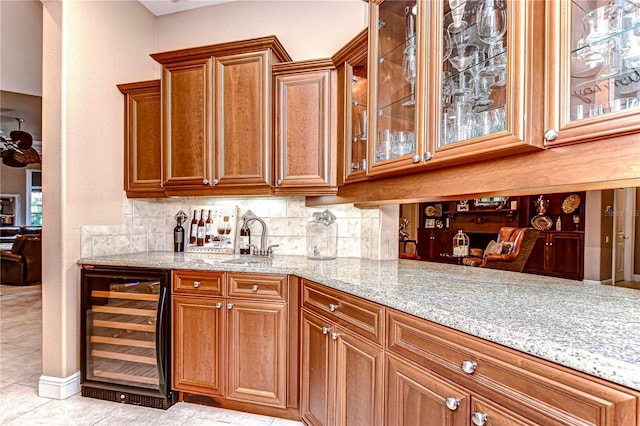 bar with backsplash, sink, light tile patterned floors, light stone counters, and beverage cooler