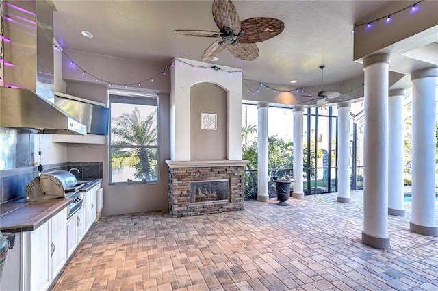 interior space with an outdoor kitchen, ceiling fan, a stone fireplace, and a grill