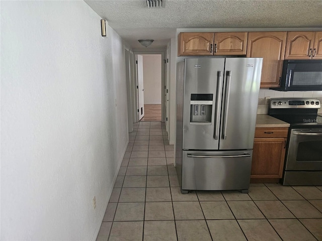 kitchen featuring tasteful backsplash, light tile patterned floors, a textured ceiling, and appliances with stainless steel finishes